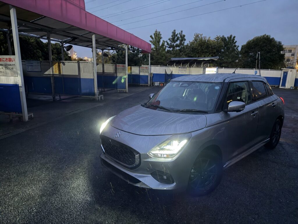 スズキ,スイフト,コイン洗車場,雨,水洗い後,外観,ヘッドライト点灯,シルバー,コンパクトカー,駐車場